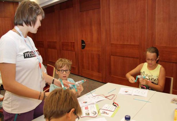 Kinder bauen unter Anleitung einer Betreuerin an kleinen elektrischen Geräten.