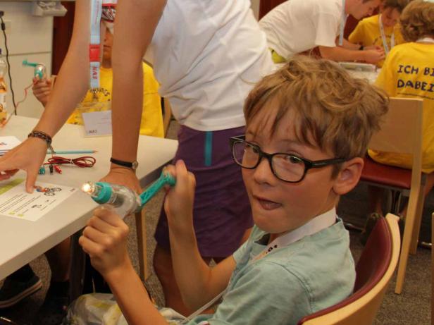 Ein Junge mit Brille bedient eine Kurbel, um eine kleine Lampe zum Leuchten zu bringen.