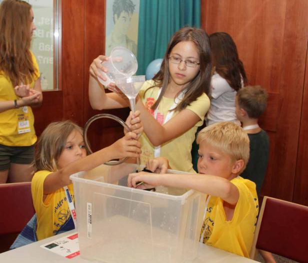 Kinder experimentieren mit Wasser und einem Trichter in einem durchsichtigen Behälter.