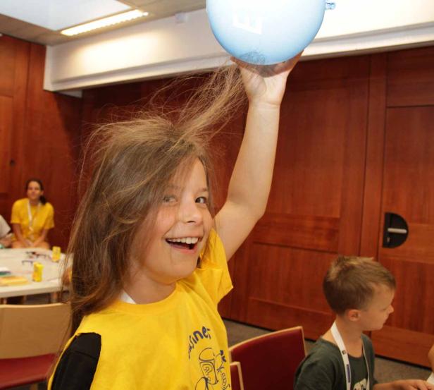 Ein Mädchen hält einen Ballon über den Kopf, wodurch sich ihre Haare statisch aufladen.