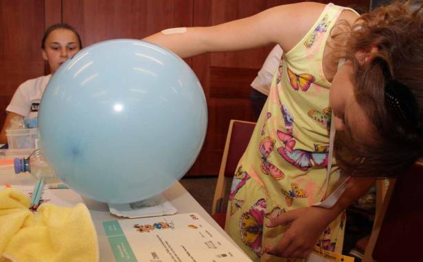 Ein Mädchen beugt sich über einen Tisch mit einem hellblauen Ballon.