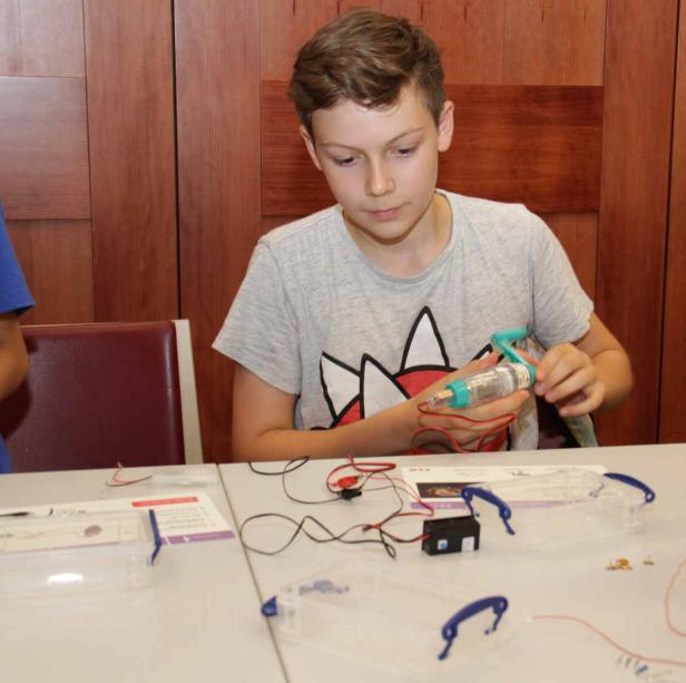 Ein Junge bastelt an einem elektronischen Bausatz mit Kabeln und Bauteilen.