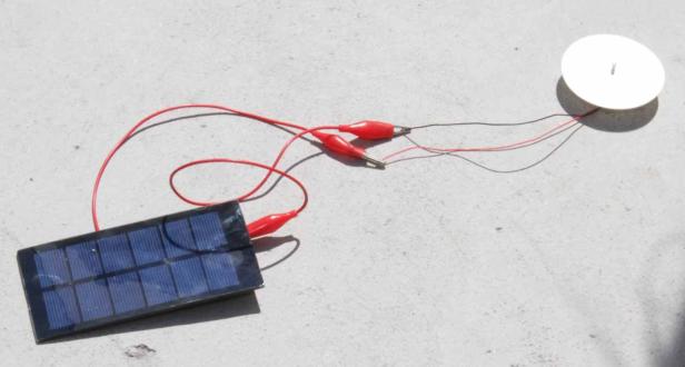 Eine kleine Solarzelle ist mit Krokodilklemmen und Kabeln an einen Summer angeschlossen.