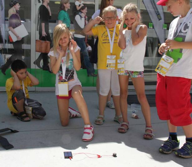 Kinder halten sich die Ohren zu, während ein Solarpanel einen Summer antreibt.