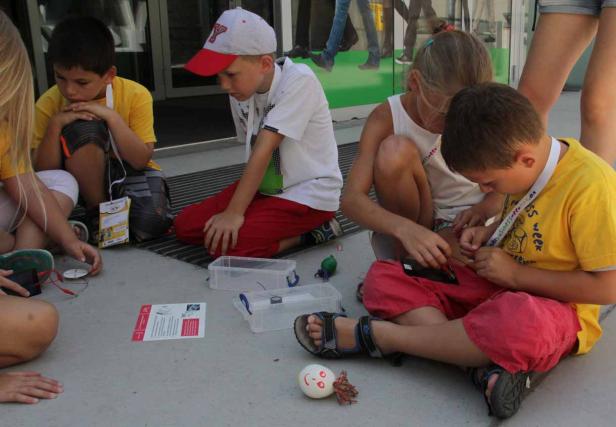 Eine Gruppe Kinder sitzt auf dem Boden und bastelt an kleinen elektronischen Projekten.
