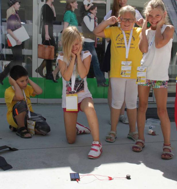 Kinder halten sich die Ohren zu, während eine Solaranlage einen Summer antreibt.