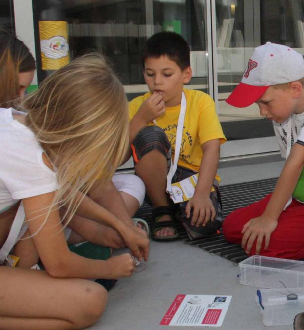 Eine Gruppe Kinder sitzt auf dem Boden und bastelt mit Elektronikbauteilen.
