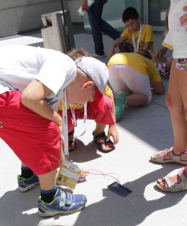 Eine Gruppe Kinder betrachtet ein Smartphone auf dem Boden.