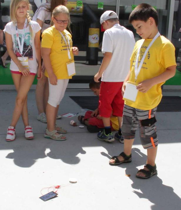 Eine Gruppe Kinder steht um ein kleines Solarpanel auf dem Boden.