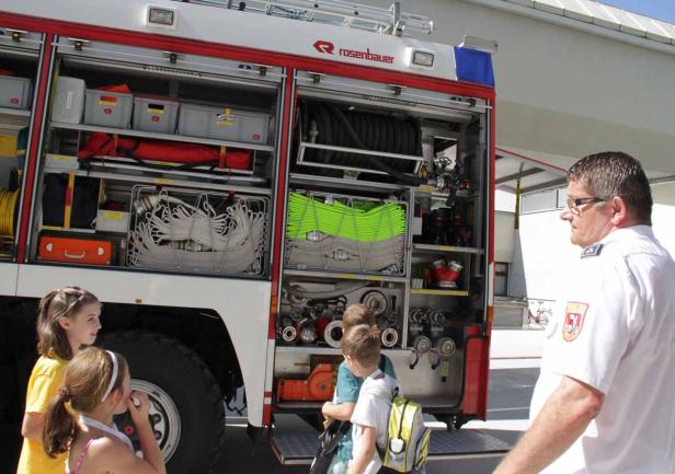 Kinder und ein Feuerwehrmann betrachten die Ausrüstung in einem Feuerwehrfahrzeug.