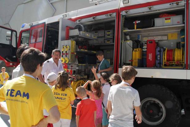 Eine Gruppe Kinder besichtigt ein Feuerwehrauto mit einem Feuerwehrmann.