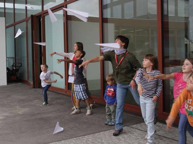 Eine Gruppe von Kindern und ein Erwachsener werfen Papierflieger.