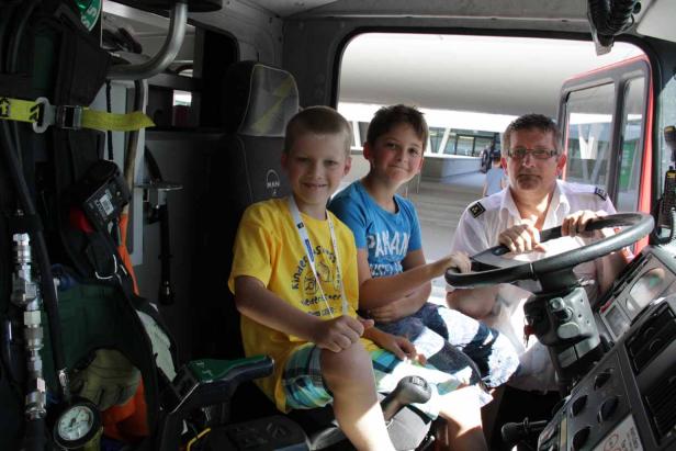 Zwei Jungen und ein Feuerwehrmann sitzen im Führerhaus eines Feuerwehrautos.