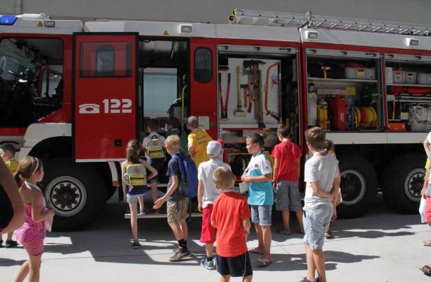 Eine Gruppe Kinder steigt in ein rotes Feuerwehrauto mit der Aufschrift „122“ ein.