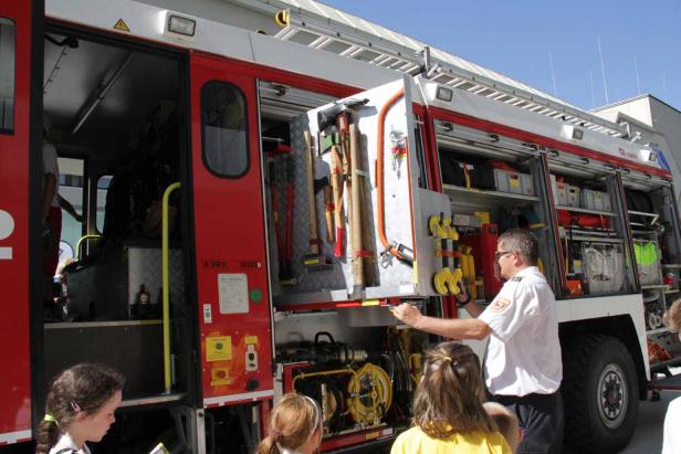 Ein Feuerwehrmann zeigt Kindern die Ausrüstung eines Feuerwehrwagens.