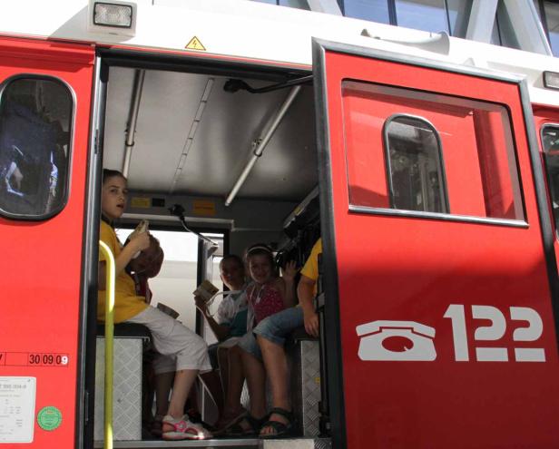 Eine Gruppe Kinder sitzt in einem roten Feuerwehrwagen mit geöffneten Türen.