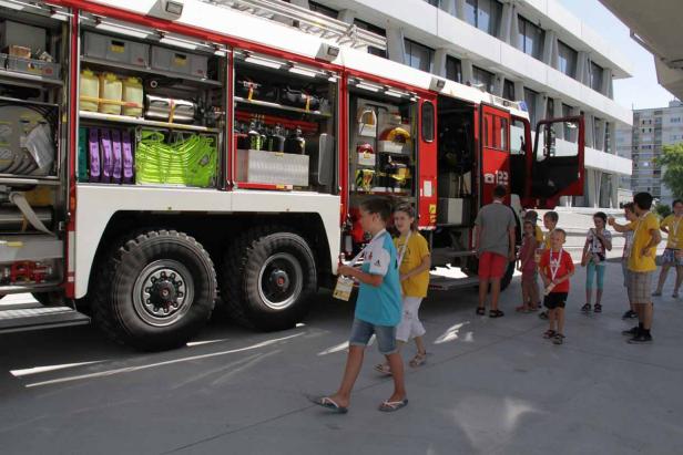 Eine Gruppe Kinder besichtigt ein rotes Feuerwehrauto mit geöffneten Fächern.