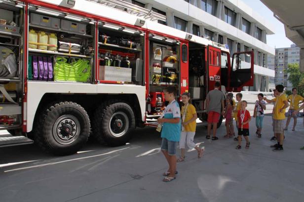 Eine Gruppe Kinder besichtigt ein rotes Feuerwehrauto mit geöffneten Fächern.