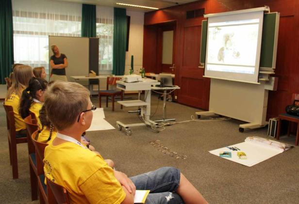 Kinder sitzen in einem Klassenzimmer und schauen auf eine Projektion an der Wand.