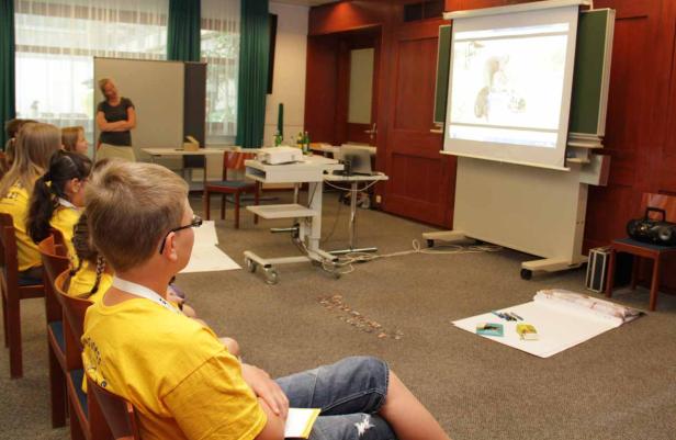 Kinder sitzen in einem Raum und schauen auf eine Projektion an der Wand.