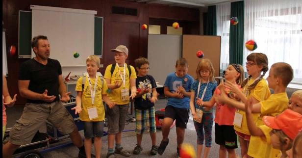 Ein Mann zeigt einer Gruppe von Kindern, wie man mit Bällen jongliert.