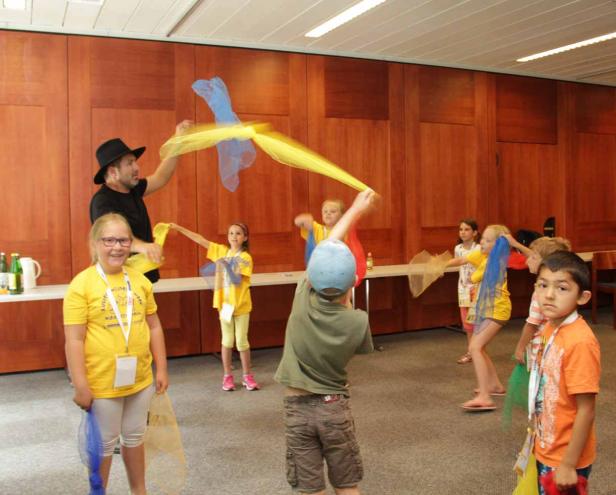 Eine Gruppe Kinder spielt mit bunten Tüchern in einem Raum.