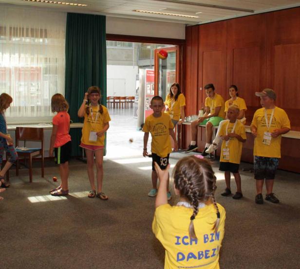 Eine Gruppe Kinder in gelben T-Shirts spielt in einem Raum mit Bällen.
