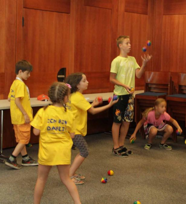 Eine Gruppe Kinder übt das Jonglieren mit bunten Bällen in einem Raum.