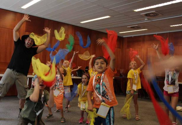 Eine Gruppe Kinder und ein Mann werfen bunte Tücher in die Luft.