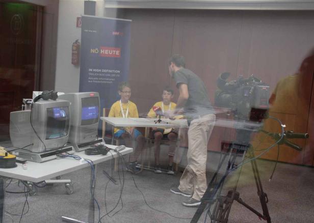 Zwei Jungen sitzen an einem Tisch vor Mikrofonen in einem Fernsehstudio von ORF NÖ Heute.