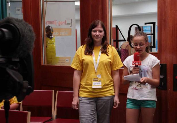 Zwei junge Frauen stehen vor einem Mikrofon des ORF und lesen einen Text ab.