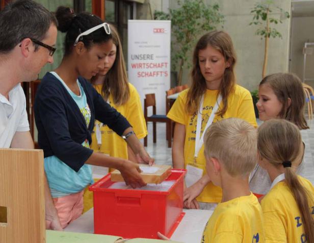 Eine Gruppe Kinder und ein Erwachsener machen Papier in einer roten Wanne.
