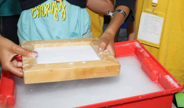 Eine Person schöpft Papier in einem roten Behälter.