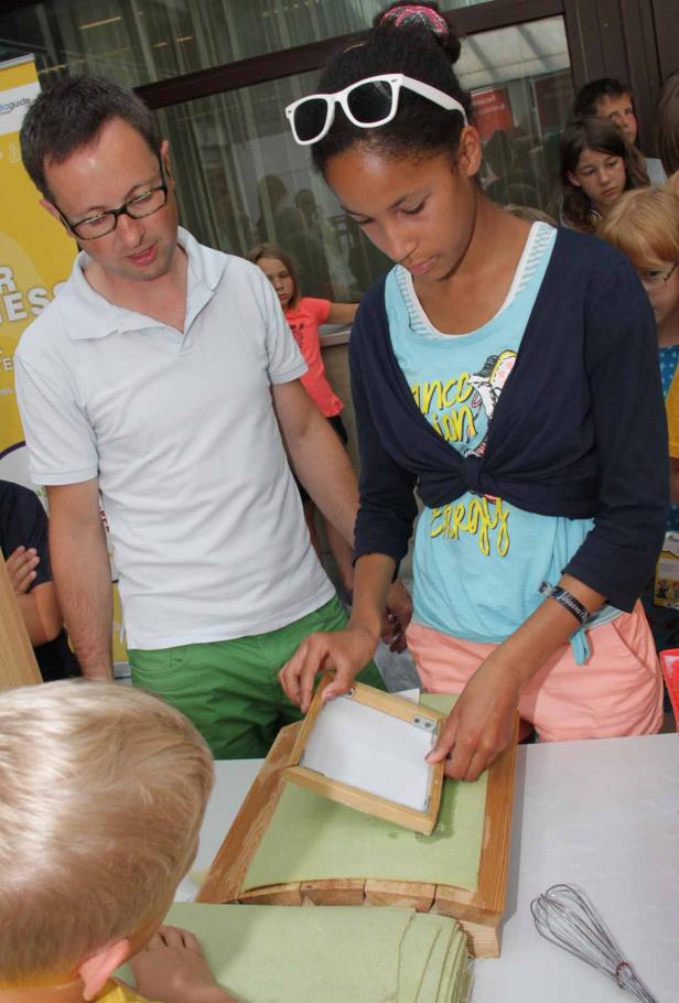 Ein Mädchen schöpft Papier unter Anleitung eines Mannes.