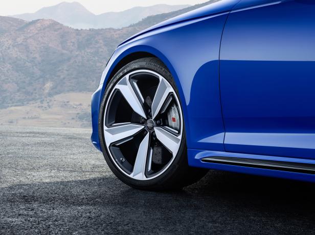 Detailaufnahme eines blauen Audi mit markanten Felgen vor einer Bergkulisse.