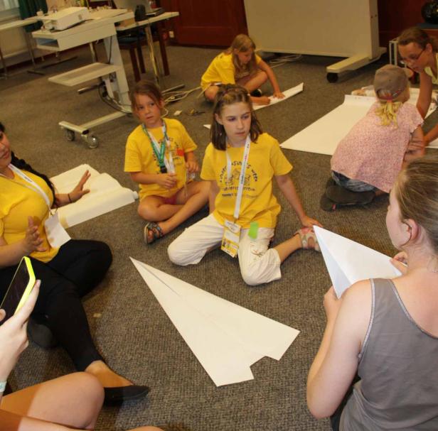 Eine Gruppe Kinder sitzt auf dem Boden und bastelt Papierflieger.