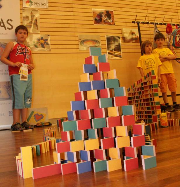 Drei Kinder stehen vor Bauwerken aus bunten Dominosteinen.
