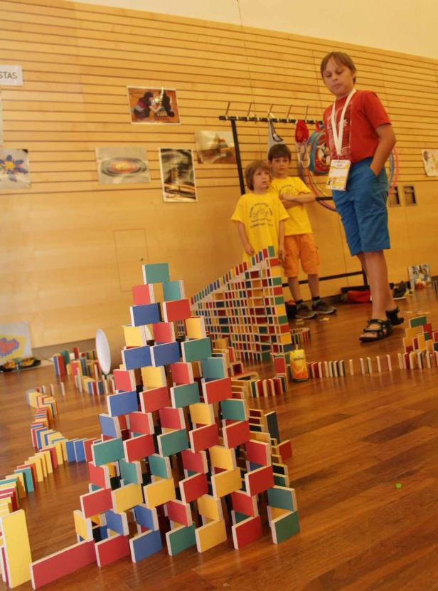 Drei Kinder stehen vor einer Konstruktion aus bunten Dominosteinen.