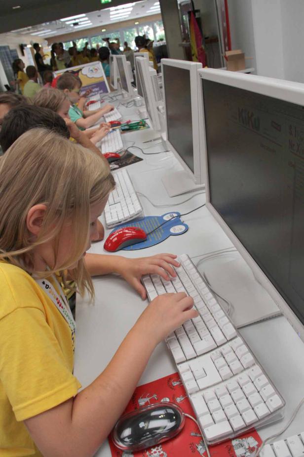 Kinder sitzen an Computern und tippen auf Tastaturen.