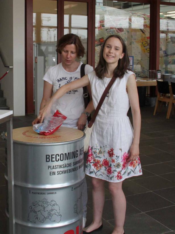 Zwei Frauen werfen Plastik in einen Behälter mit der Aufschrift „Becoming AE“.