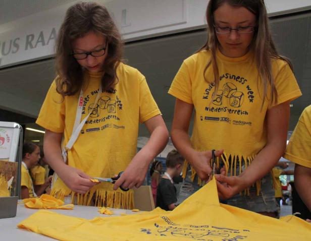 Zwei Mädchen mit gelben T-Shirts schneiden Fransen in Stoff.