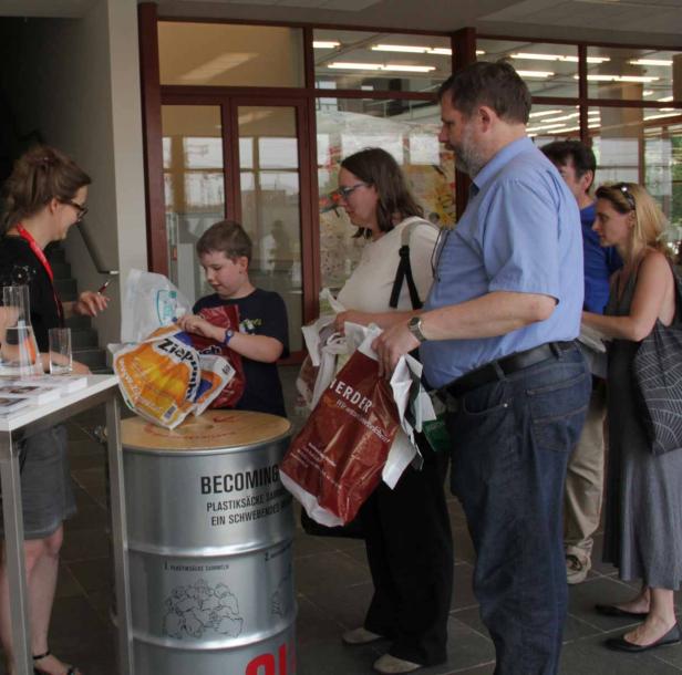 Menschen stehen an einem Stand mit einem Behälter für Plastiktüten.