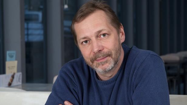 Ein Mann mit Bart und blauem Pullover schaut in die Kamera.