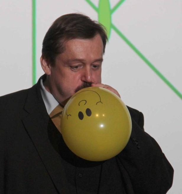Ein Mann im Anzug bläst einen gelben Ballon mit einem aufgemalten Gesicht auf.