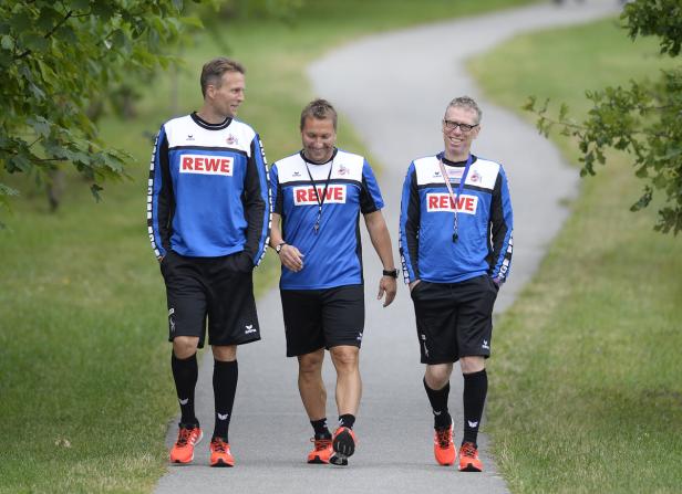 Drei Männer in Sportkleidung des 1. FC Köln gehen auf einem Weg entlang.