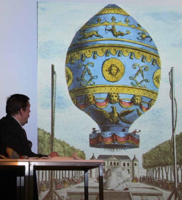 Ein Mann sitzt vor einer Projektion, die einen historischen Heißluftballon zeigt.
