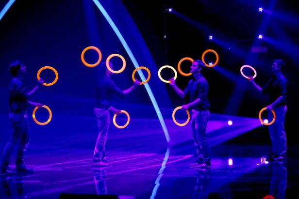 Vier Jongleure treten mit leuchtenden Ringen auf einer Bühne auf.