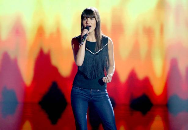 Eine junge Sängerin tritt mit einem Mikrofon vor einem farbenfrohen Hintergrund auf.