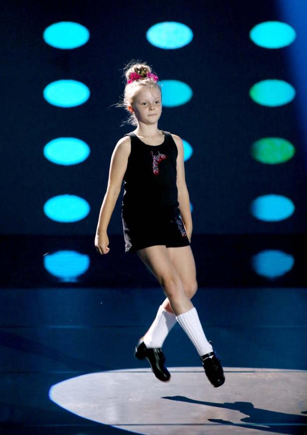 Ein junges Mädchen tanzt in traditioneller irischer Kleidung auf einer Bühne.