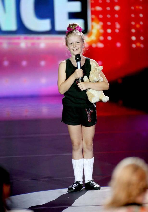 Ein junges Mädchen steht mit einem Mikrofon und einem Stofftier auf einer Bühne.